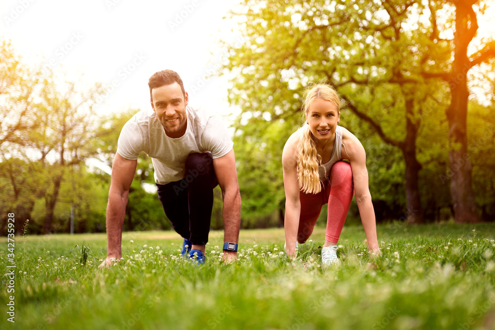 Fototapeta premium Fit young man and woman exercising in park. Smiling caucasian couple doing workouts on grass on sunny morning.