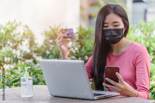 Beautiful young asian woman wearing a protective face mask hold while mobile phone paying with credit card for online shopping item