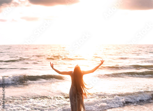Photographie happy woman stands seashore turned away hand raised to heaven sky sun light
