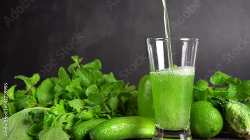 Pouring mixed green vegetables with fruits juice into a glass and fresh vegetables background.