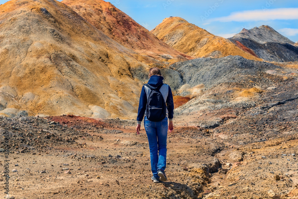 Hiking concept. Young woman goes walks among the hills, view from the back. Landscape like a planet Mars surface. Solidified red-brown black Earth surface. Copy space for text