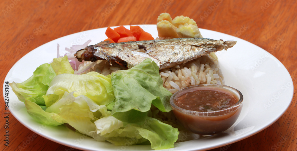 Breakfast in the white round plate. Fried mackerel and Rice with Spicy Shrimp Paste Dip and vegetable, Chinese cabbage, baby corn, carrots and sliced onions.