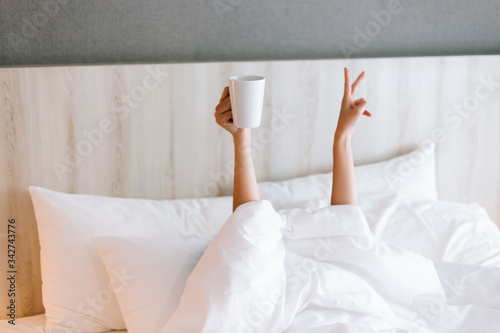 Female hand holding a cup of coffee while lying down on bed. Coffee morning concept photo