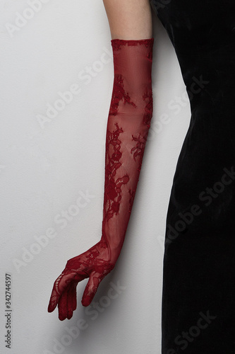 Cropped shot of a lady in a black tight dress and a burgundy evening glove against the gray wall. The elegant elbow glove is made of the lace fabric with floral pattern. 