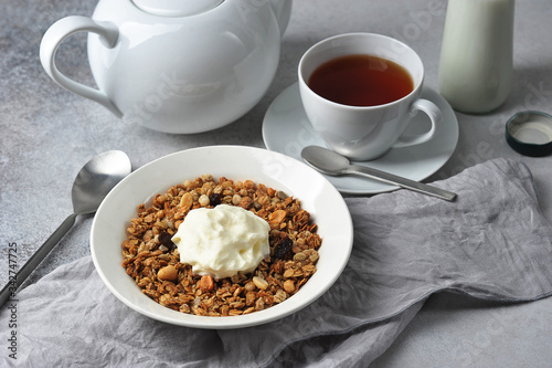 Muesli with nuts, seeds and raisins.  A cup of tea and a bottle of milk complete the composition.  Light background.  Close-up.