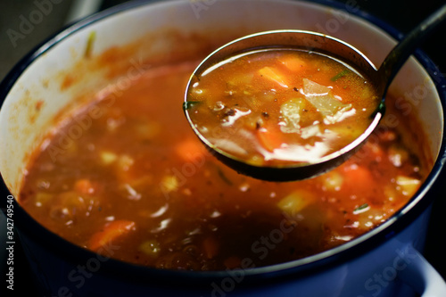 Cabbage soup. Blurred cooking pot on background. Focus in ladle.