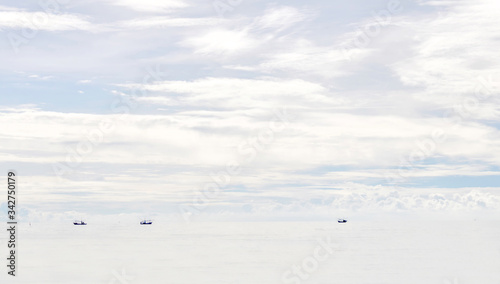 Cloudy white sky and white sea with little black spots of fisherman ships