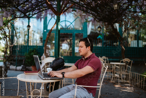 A young caucasian man is working on a computer in a cafe garden