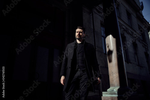a man in a black suit walks along the historical streets of the city