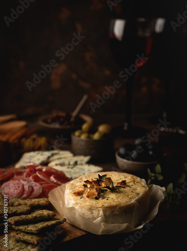 baked camembert cheese with jam, sausage, blue cheese, olives and snacks, on a wooden board, glasses with red wine
