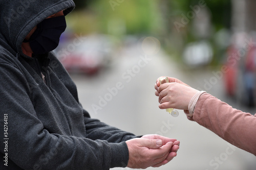 Close-up of an older man in a dark hoodie and young woman's hands apllying hand sanitizer gel on the hands of an older man.