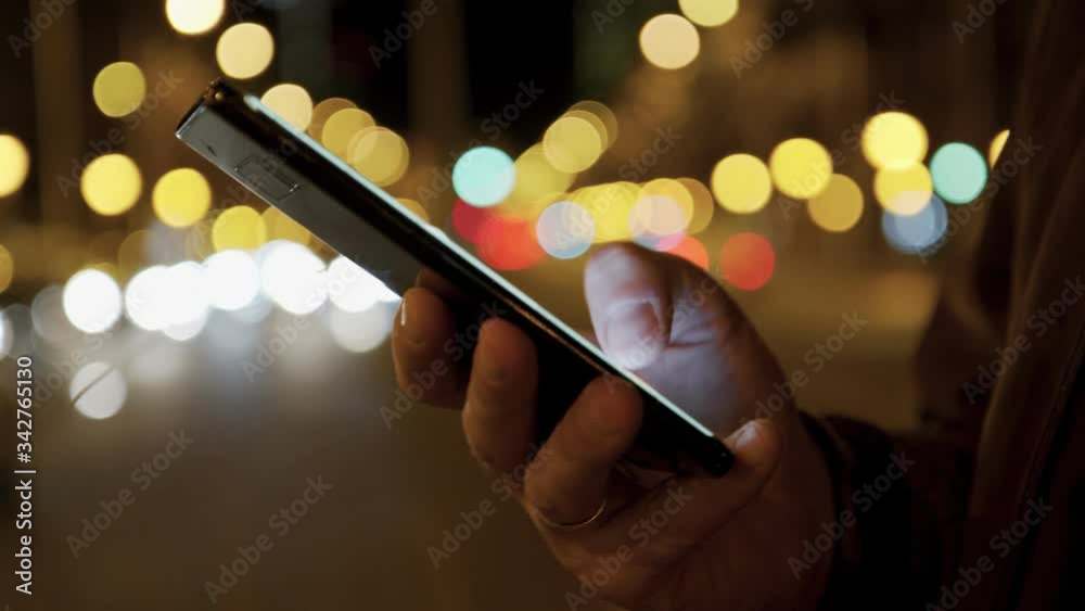 Man hands typing text message smartphone at night city street. Connecting and searching of social network. Blurred background and bokeh effects. Handheld close-up shot. 4K UHD.