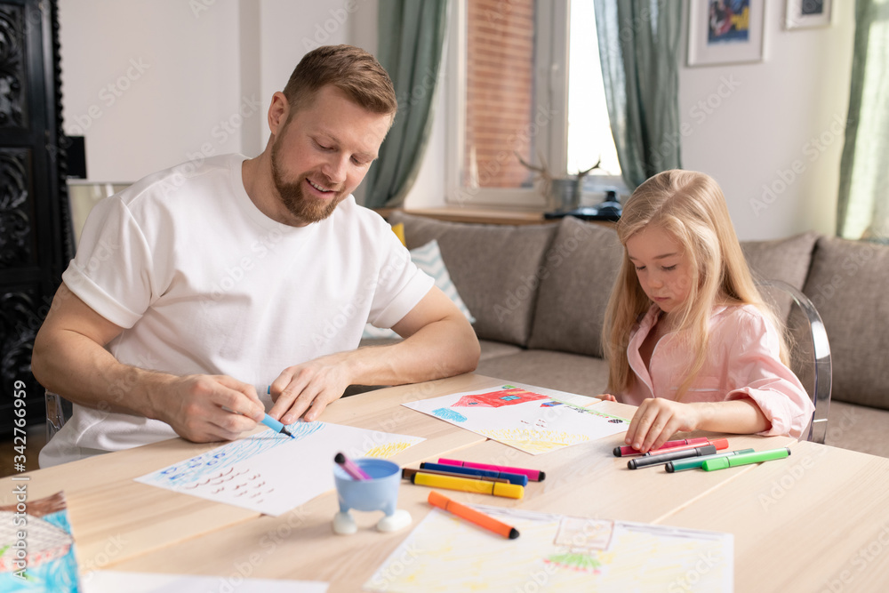 Happy young man and his little cute daughter drawing by table in living-room Happy young man and his little cute daughter drawing by table in living-room