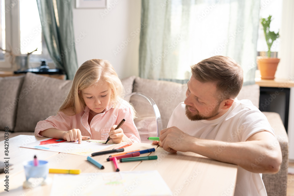 Happy young father in casualwear looking at his cute little daughter drawing Happy young father in casualwear looking at his cute little daughter drawing