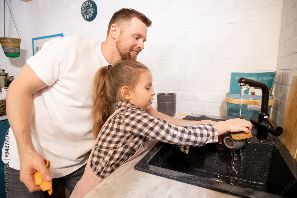 Happy young father standing by his little daughter and helping her to wash cup Happy young father standing by his little daughter and helping her to wash cup