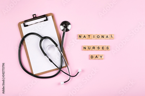 National Nurse Day Holiday Background. Medical stethoscope, white clipboard notebook and wooden letters text. Healthcare medicine concept. Top view, flat lay.