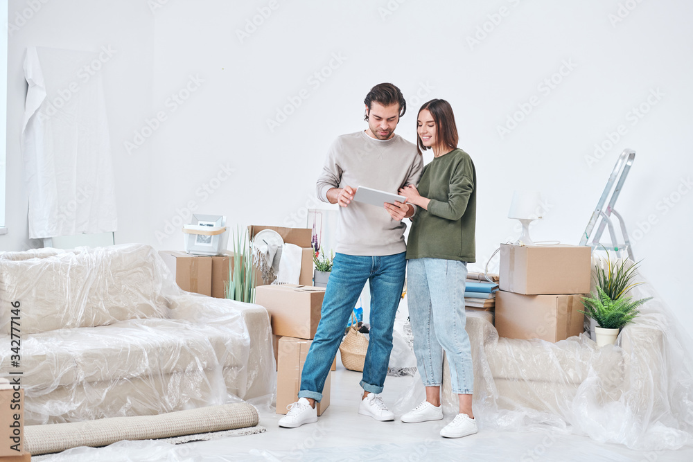 Young affectionate man and woman in casualwear looking at digital tablet display Young affectionate man and woman in casualwear looking at digital tablet display