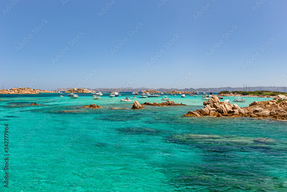 Various tourist boats are stationed in the clear and transparent waters in the Maddalena archipelago in Sardinia, Italy.