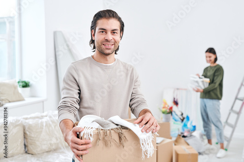 Happy young man in light grey sweatshirt holding box with scarves or plaids