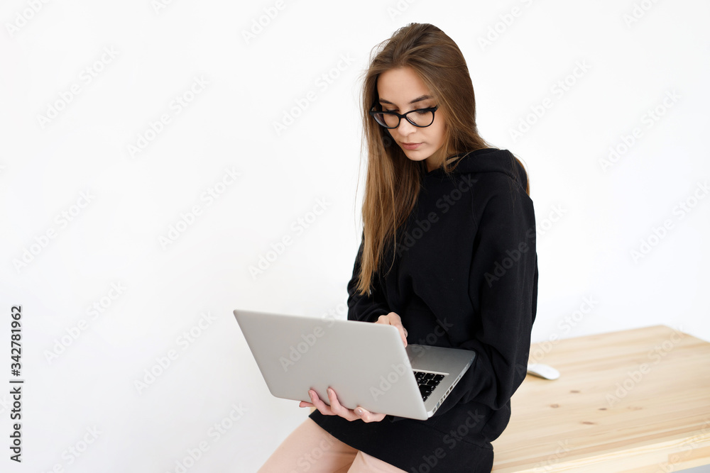 Young woman freelancer girl in glasses using a laptop at a table on a white background, communicates on the Internet Young woman freelancer girl in glasses using a laptop at a table on a white background, communicates on the Internet
