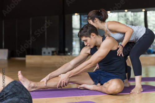 Young Yoga techer lady helping her Caucasian studen streching the muscle in the Yoga class.