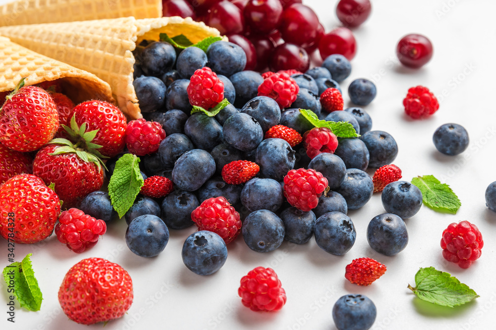 Fresh summer berries with mint in waffle ice cream cones on white marble background Fresh summer berries with mint in waffle ice cream cones on white marble background