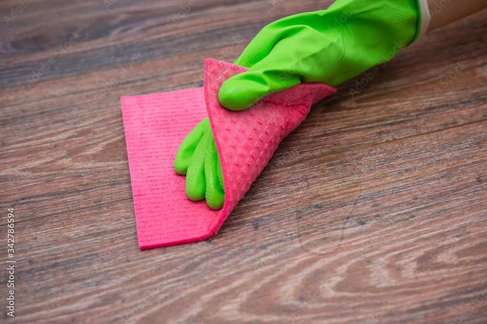 Closeup of a hand in a green rubber glove rubbing a wet wooden surface. The concept of disinfection of premises, the prevention of viral and bacterial diseases. Cleaning wooden surfaces. Closeup of a hand in a green rubber glove rubbing a wet wooden surface. The concept of disinfection of premises, the prevention of viral and bacterial diseases. Cleaning wooden surfaces.