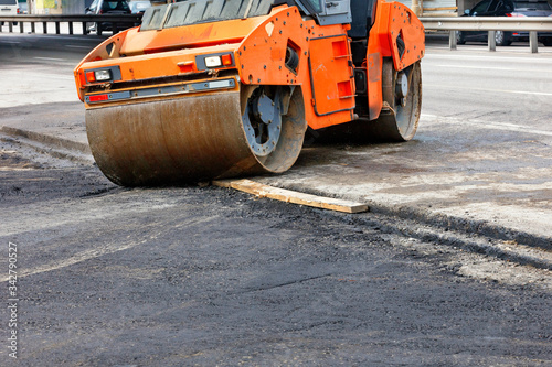 A large road vibratory roller rolls off the highway to lay fresh asphalt on the new road.