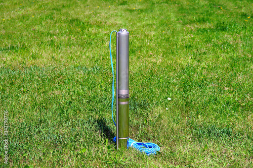 Well pump with cable on a background of green grass. Pump in the nature.