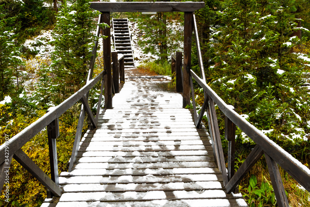 forest bridge over river with wooden railings under first snow, danger ice on bridge