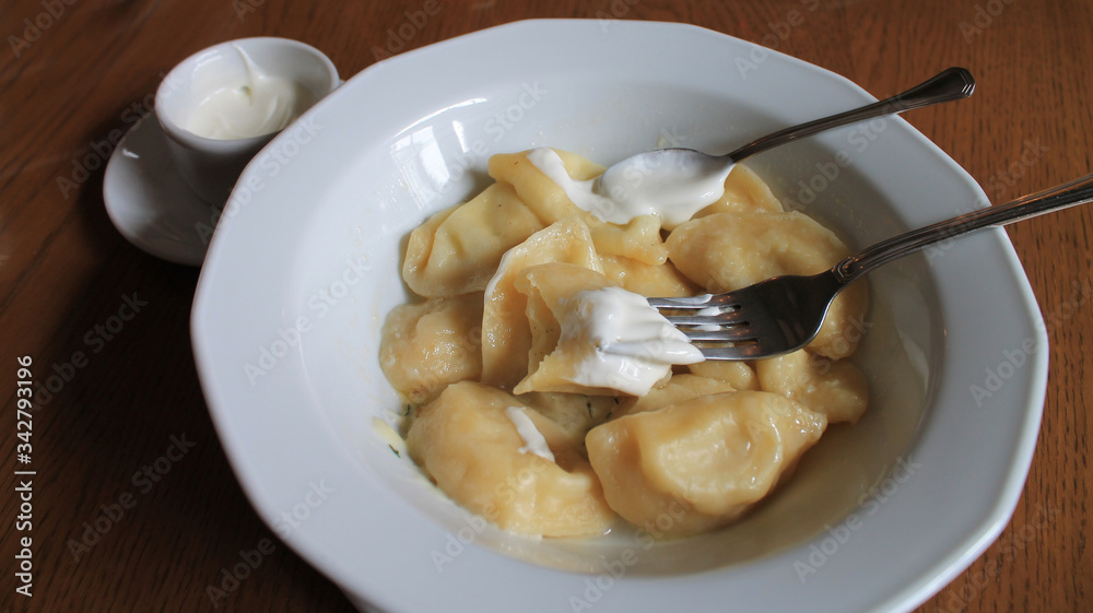 Dumplings with cottage cheese in a white plate with sour cream
