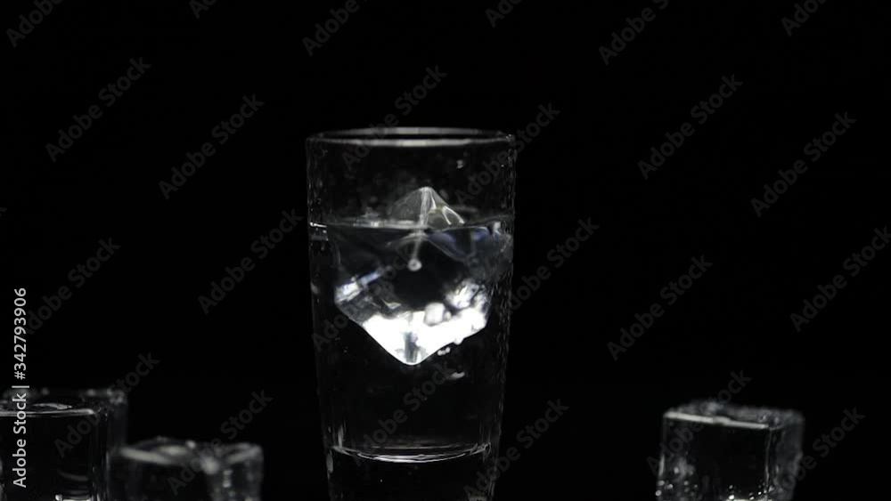 Add ice cube to shot of vodka in glass against black background. Alcohol drink Add ice cube to shot of vodka in glass against black background. Alcohol drink