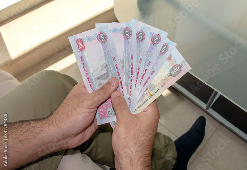 UAE national currency. UAE money banknotes. Young man holds in hands  dirhams paper money.  photo