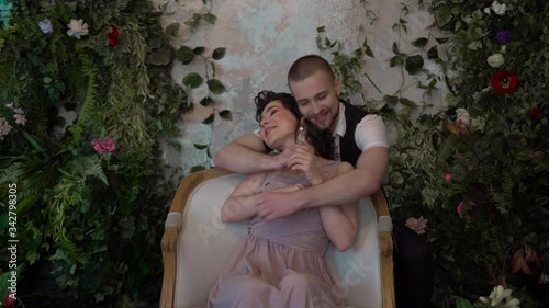 a beautiful girl sits on a chair against the background of the garden, and behind her a brutal man hugs her. A woman is worried from the beginning, and then she is happy and she loves each other
