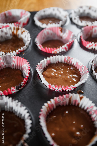 
A muffin baking dish in which there are paper inserts with chocolate dough inside. Homemade cakes for children and adults