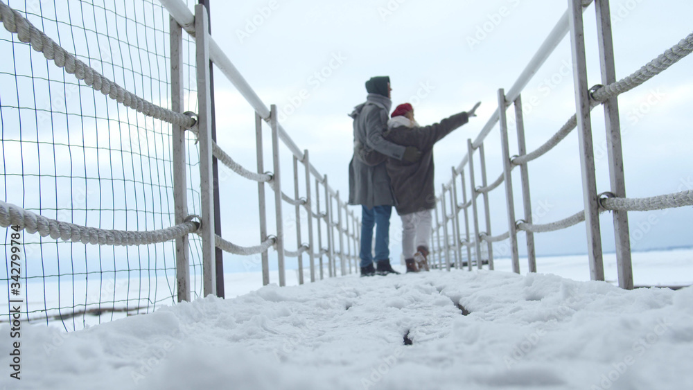 A couple hugs and walks on a frozen bridge