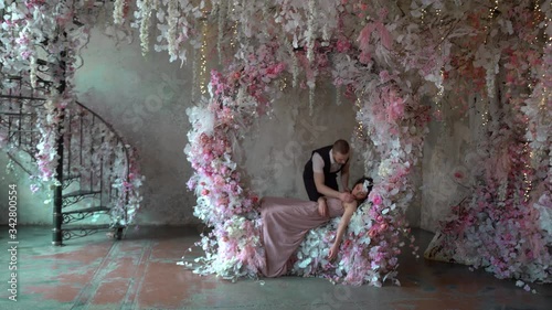 man, a prince from fairy tale about snow white, runs to the princess to kiss her. There are many flowers around. A man ran through the stairs and the ground, the girl lies unconscious agains