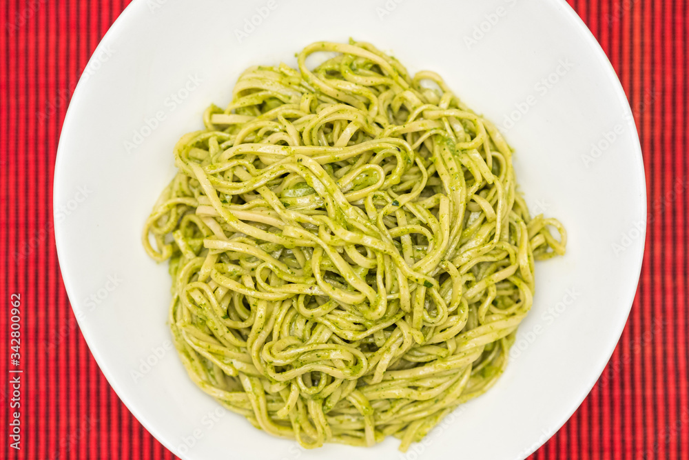 Homemade pasta noodles with green pesto on red background Homemade pasta noodles with green pesto on red background