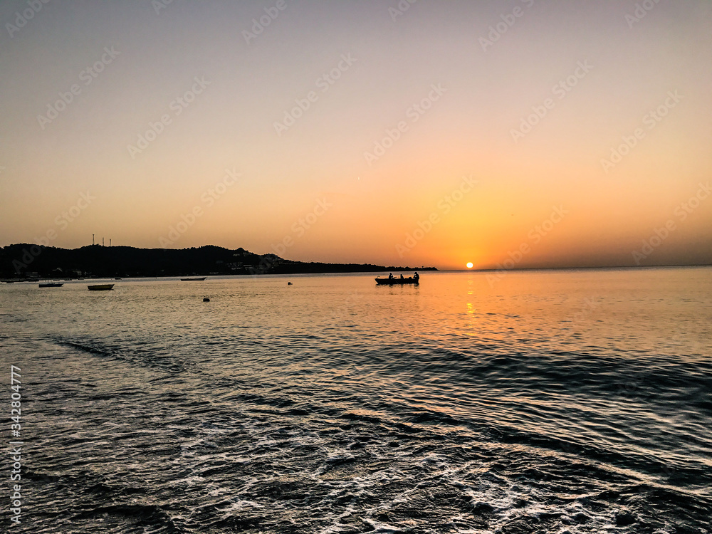 Orange and Pink Sunset with boat and Mountain Silhouette at Grand Anse Bay St Georges, Grenada Orange and Pink Sunset with boat and Mountain Silhouette at Grand Anse Bay St Georges, Grenada