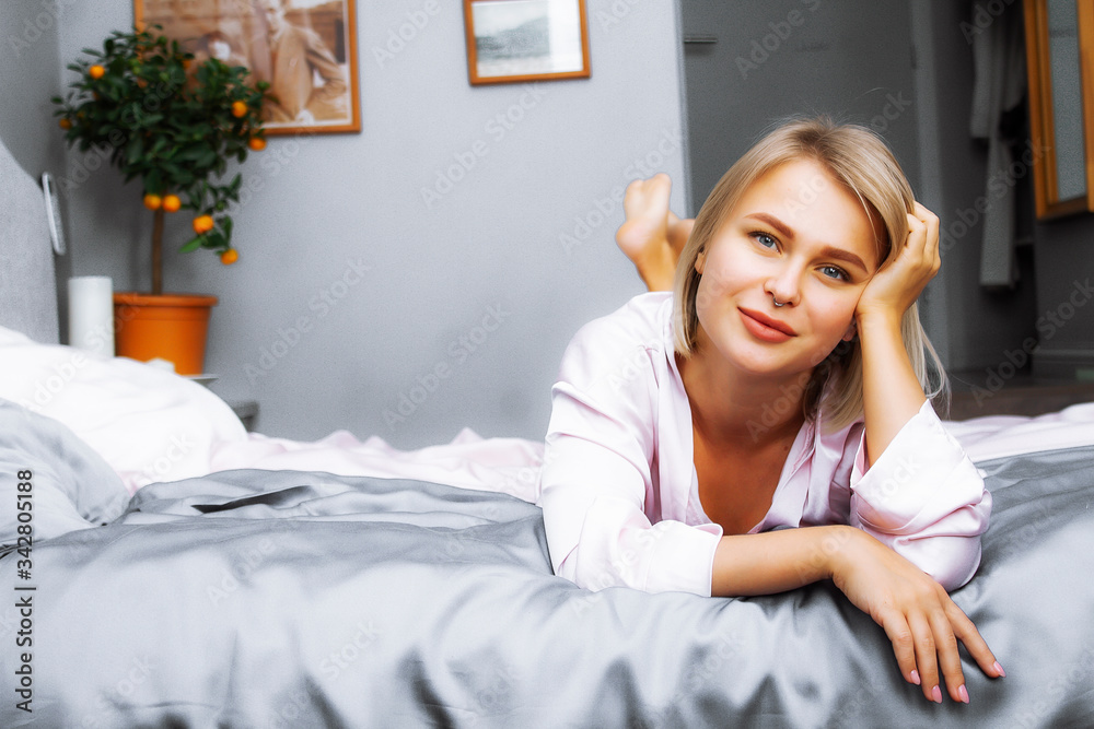 Beautiful woman in a silk dressing gown lies in bed. Blonde on satin  bedding. Pink silk bathrobe. Stock-foto | Adobe Stock