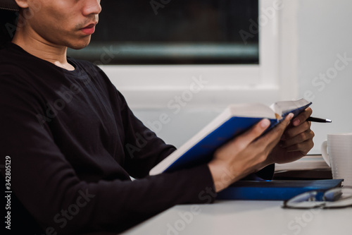 Young man reading book at work desk late at night, Knowledge and learning concept.