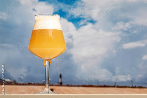 Photography A hazy India pale ale beer in a Teku beer glass on a table with a tropical clouded sky background