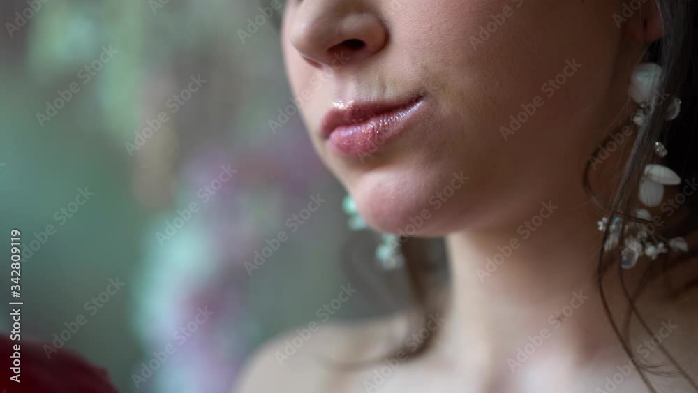 the girl s lips bite and eat a red apple. The woman s face is close-up, only her mouth. The jaw opens and eats food. The teeth bite the fruit. The lips are painted with lipstick.