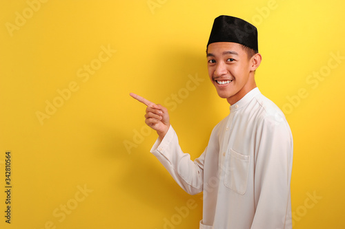 Happy Young Asian muslim man pointing to showing a copy space presenting something