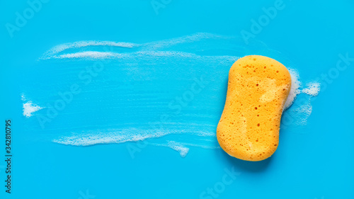 Yellow washing sponge in soap foam on a blue background isolated photo