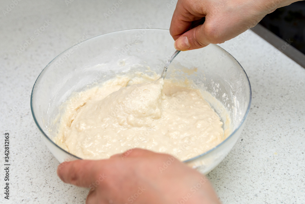 Woman's hands with an yeast dough. The woman is stirring the baking dough in a glass bowl.