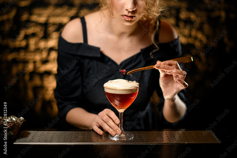 female bartender neatly decorates glass with foamy cocktail.