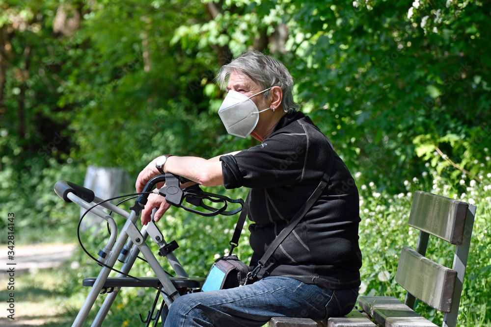 seniorin mit atemschutzmaske sitzt in einem park