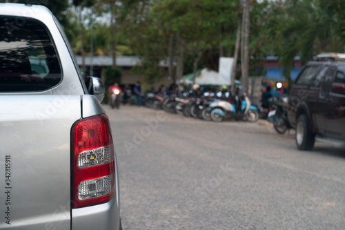 Rear side of pickup car stop on asphalt road beside with blurred of cars parking arear and local market.