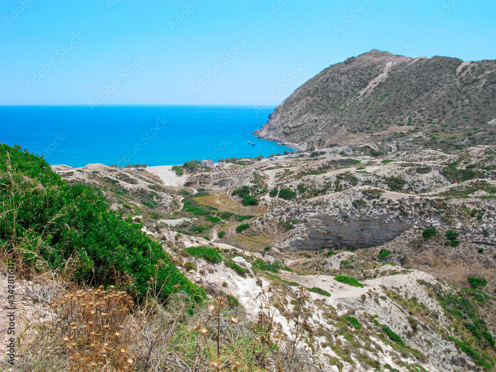 Greece, Cyclades, Milos island. Panoramic view. Mountain ridges, calm sea, clear blue sky and prickly plants on a cliff.